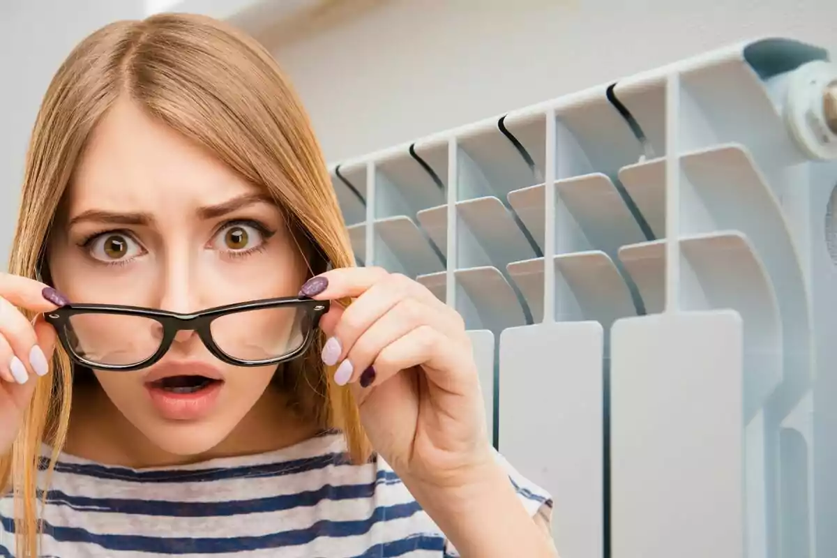 Mujer sorprendida mirando a través de sus gafas frente a un radiador.